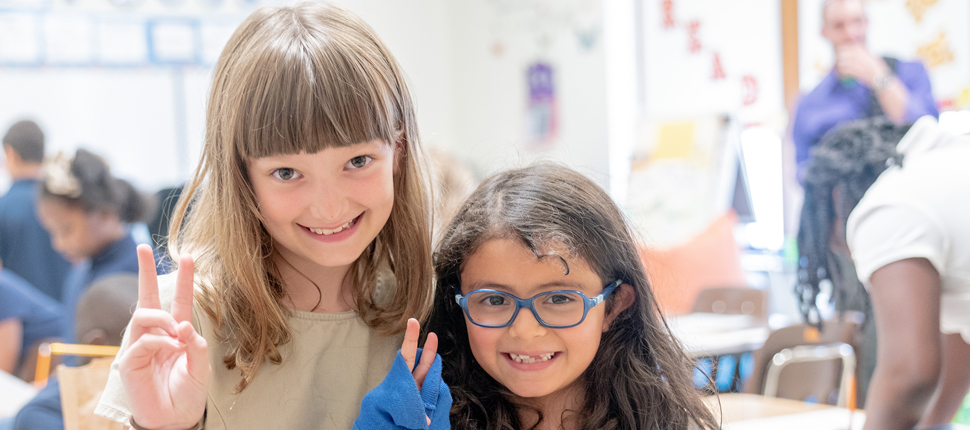 Elementary school girls holding up peace sign and smiling