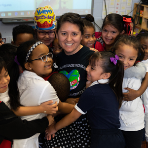 Many young students hugging teacher